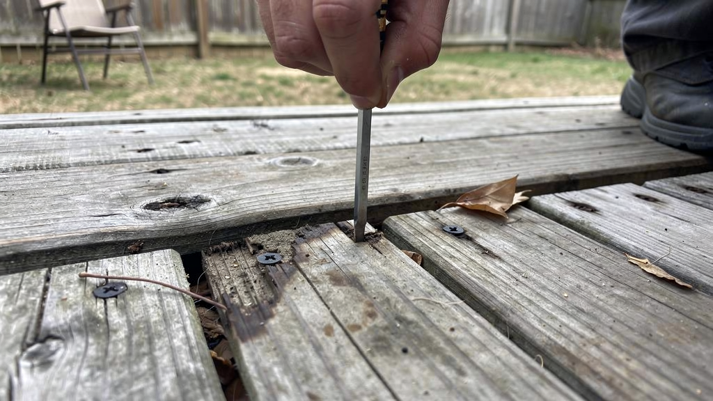 Weathered residential deck boards being checked for soft spots