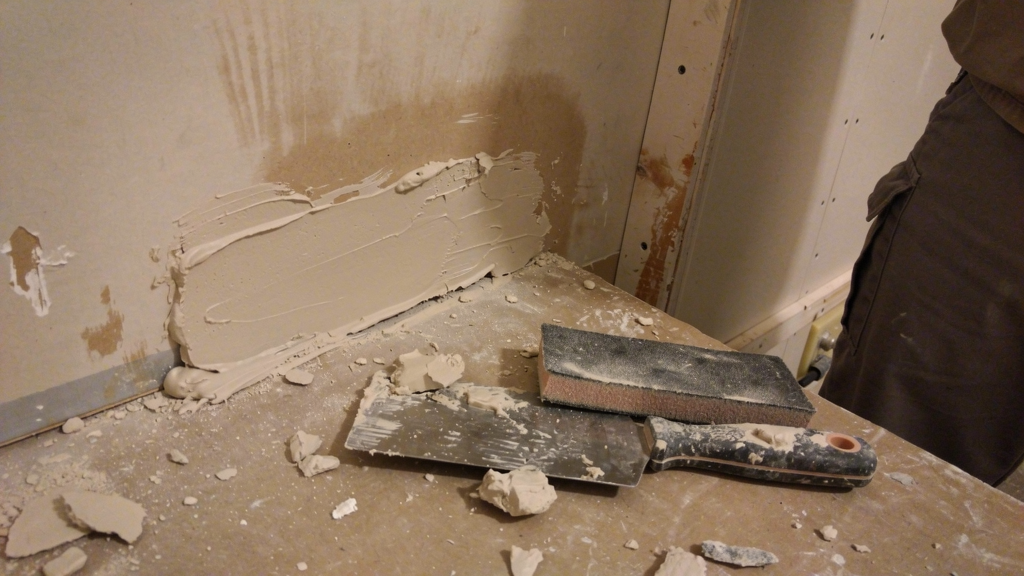 Drywall patch and joint compound being prepared on a work surface