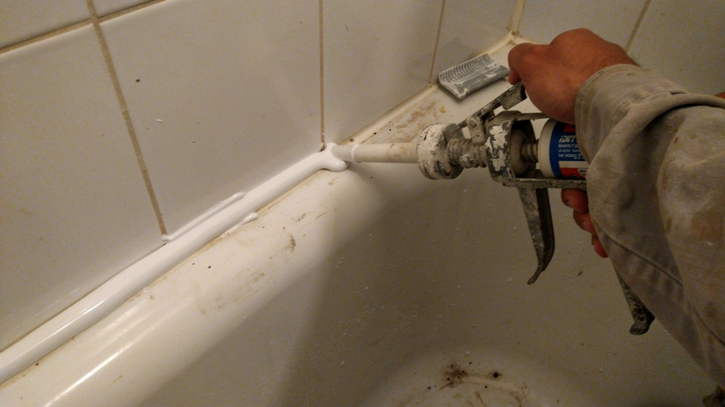 Fresh bathroom caulk being applied along a shower joint