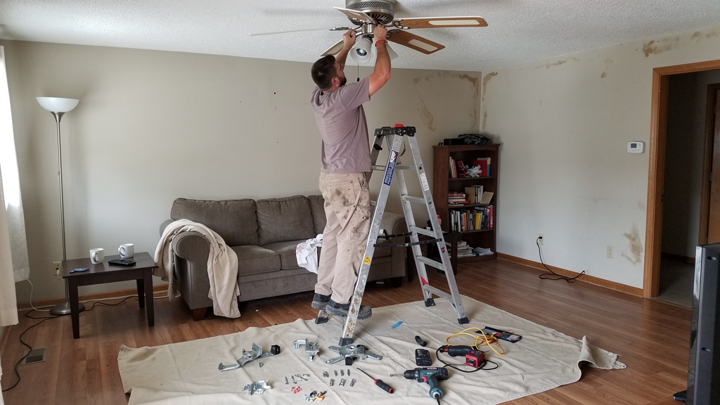 Handyman installing a ceiling fan in a residential room