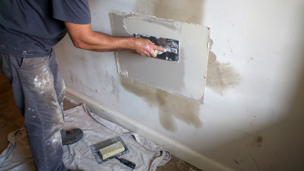 Handyman applying joint compound to a drywall patch on an interior wall