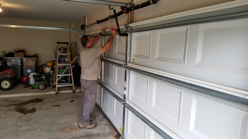 Handyman inspecting a residential garage door track and hardware