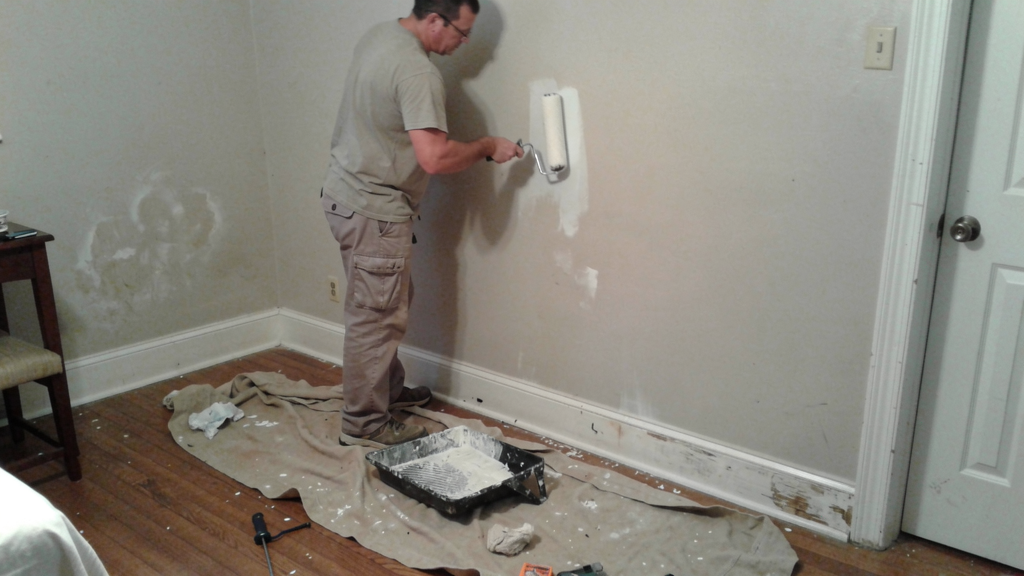 Handyman carefully painting an interior wall near trim in a lived-in home