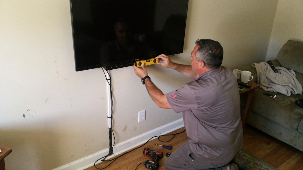Handyman leveling a wall-mounted television in a living room